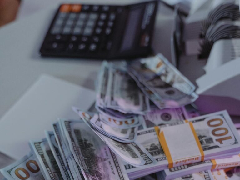 A close-up view of stacked US dollar bills next to a calculator and money counter.