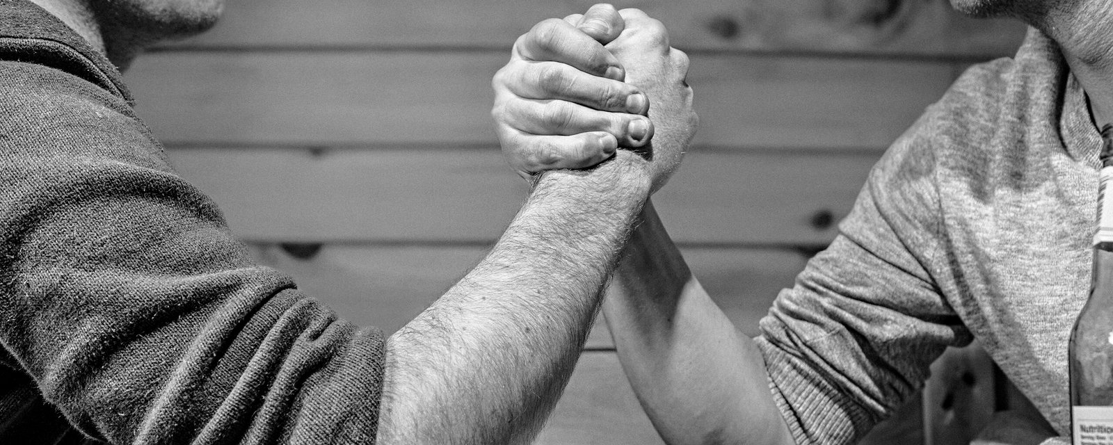 Two men engage in a high-stakes arm wrestling match surrounded by money on a table.